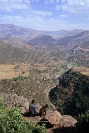 Image du Maroc Professionnelle de  Un berbère accompagné de sa chèvre assis sur des rochers qui surplombent un paysage d'une des vallées du Haut Atlas sur la route à travers  la montagne qui mène de Marrakech à Ouarzazate le Dimanche 24 Août 1997. (Photo / Abdeljalil Bounhar)
